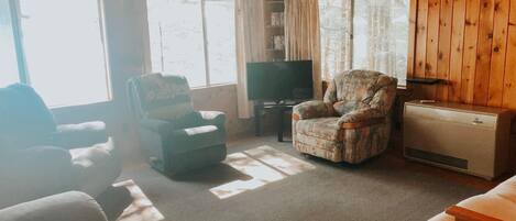 A cozy living room with a large window, a television, and two armchairs.
