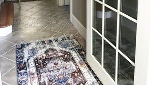 A hallway with a decorative wreath on the door, a rug, and a kitchen in the background. - Walk to Death Valley! | Cozy Lakeside Suite (Clemson)
