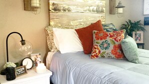 A neatly arranged bedroom with a bed, pillows, a nightstand, a wall clock, and a framed photo. - Walk to Death Valley! | Cozy Lakeside Suite (Clemson)