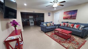 A living room with a blue sofa, red coffee table, and a red side table with magazines. There is a kitchen in the background with a microwave and oven. - COZY Private APARTMENT "3Bedroom/1Bathroom" (Conyers)