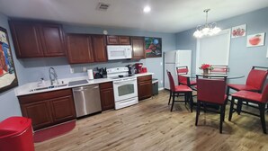 A kitchen with wooden cabinets, a microwave, a stove, and a dining area with red chairs. - COZY Private APARTMENT "3Bedroom/1Bathroom" (Conyers)