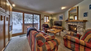 A cozy living room with a fireplace, a television, and a large window overlooking a snowy landscape.