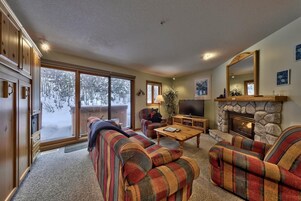Un salón acogedor con chimenea, televisor y un ventanal grande con vistas a un paisaje nevado.