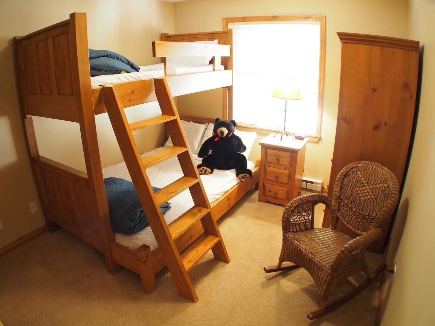 Een slaapkamer met een stapelbed, een klein nachtkastje, een stoel en een raam met jaloezieën.