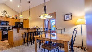 Une cuisine avec des meubles en bois, un four à micro-ondes et une cuisinière. On y trouve une table à manger avec des chaises et une lampe.