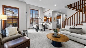 A spacious living room with a large sofa, a coffee table, and a staircase. - Trappers Landing #05 By Bear Country (Sun Peaks)