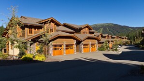 A large log cabin-style building with multiple garage doors, surrounded by a driveway and greenery. - Woodhaven #32 By Bear Country (Sun Peaks)