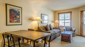 A cozy living room with a wooden dining table, two sofas, and a small coffee table. There are two lamps on the side tables, and a framed painting on the wall. - Fireside Lodge #413 By Bear Country (Sun Peaks)
