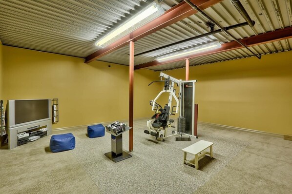 A gym with exercise equipment, a television, and a small bench.