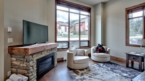 A living room with a stone fireplace, a flat-screen TV, two armchairs, and a rug.