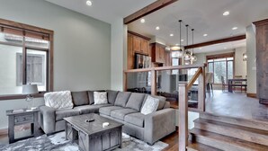 A modern living room with a sectional sofa, a coffee table, and a staircase leading to a dining area.