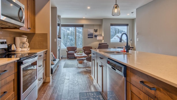 A modern kitchen with a central island, wooden cabinets, and a large window offering a view of snow-covered trees. - Echo Landing#02 (Sun Peaks)