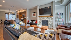 A modern living room with a fireplace, a kitchen area, and a dining space. - Echo Landing#02 (Sun Peaks)