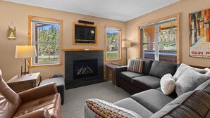 A cozy living room with a fireplace, leather sofas, and large windows offering scenic views. - Crystal Forest #22 By Bear Country (Sun Peaks)