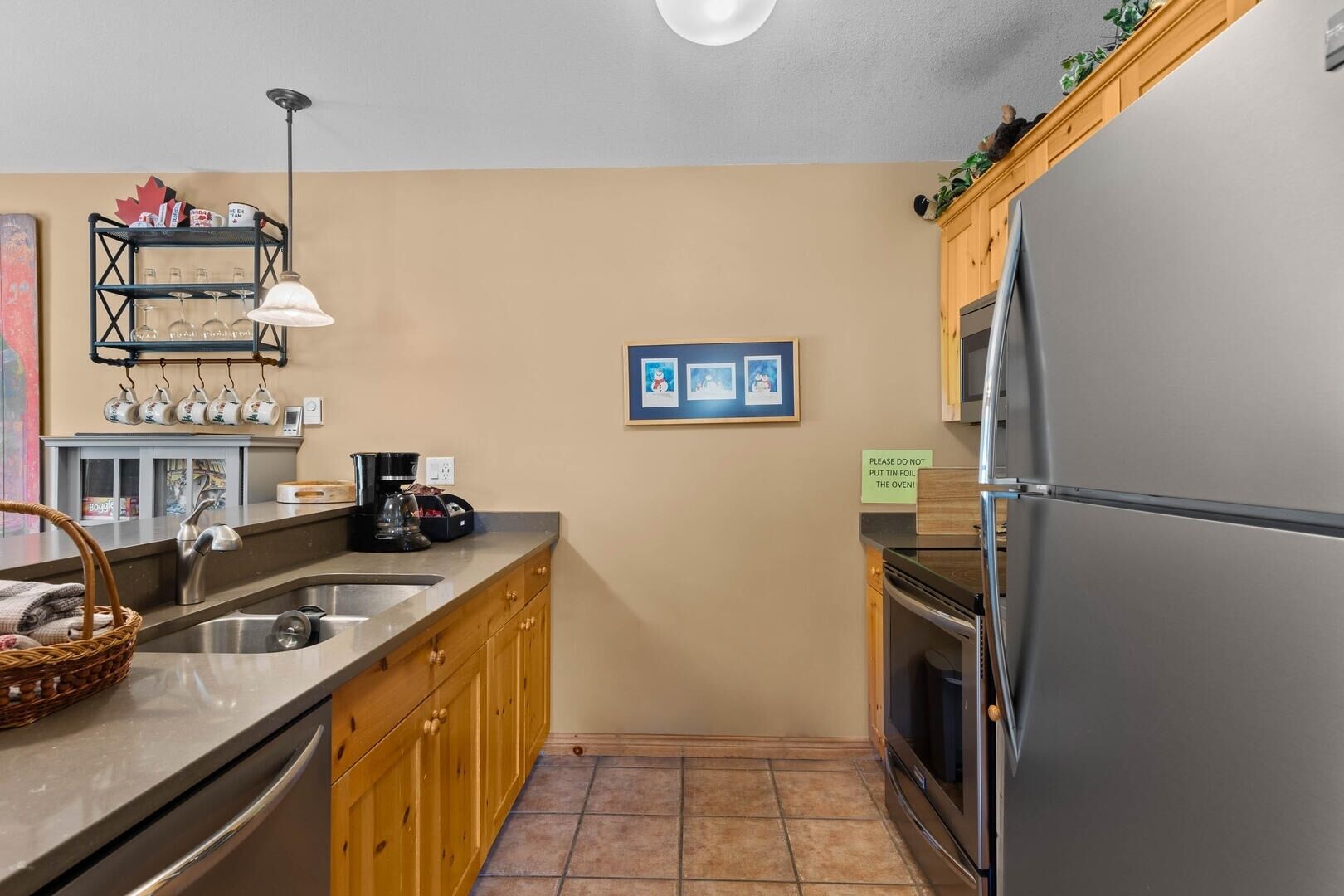 A compact kitchen with a stainless steel refrigerator, wooden cabinets, a coffee maker, and a sink.