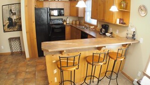 A kitchen with wooden cabinets, a black refrigerator, a stove, a microwave, and a sink. There are three bar stools and pendant lights above the counter.