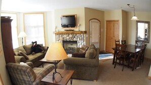 A living room with a fireplace, a television mounted above it, and a dining area with wooden furniture.
