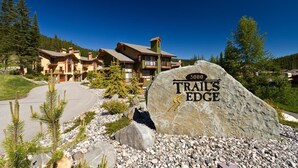 A lodge with a stone sign reading "5000 TRAILS EDGE" surrounded by a gravel driveway and pine trees. - Trails Edge #25 By Bear Country (Sun Peaks)
