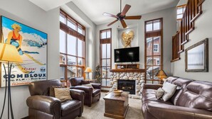 A spacious living room with leather sofas, a stone fireplace, and a large TV. - Trappers Landing #11 (Sun Peaks)