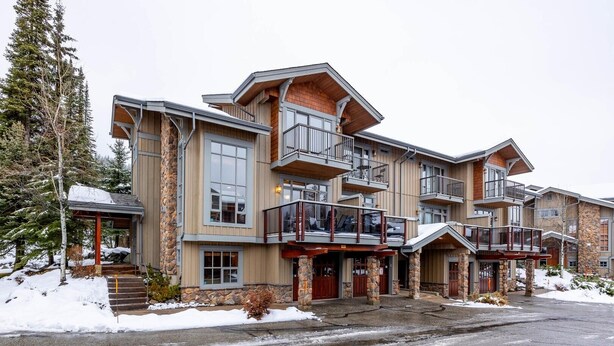 A multi-story lodge with a stone facade, multiple balconies, and a covered entrance. - Trappers Landing #11 (Sun Peaks)
