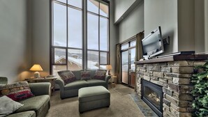 A spacious living room with a fireplace, large windows, and a cozy seating area. - Stones Throw #56 By Bear Country (Sun Peaks)