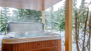 A hot tub in a covered outdoor area with a view of snow-covered trees. - Snow Creek Village #48 By Bear Country (Sun Peaks)