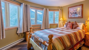 A bedroom with a large bed, wooden headboard, and multiple windows with curtains. - Snow Creek Village #48 By Bear Country (Sun Peaks)