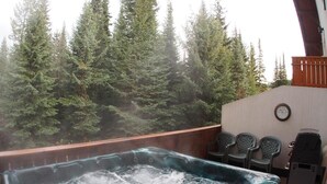 A hot tub with a view of a forest. There are chairs and a grill on the patio. - Timberline Village #38 By Bear Country (Sun Peaks)
