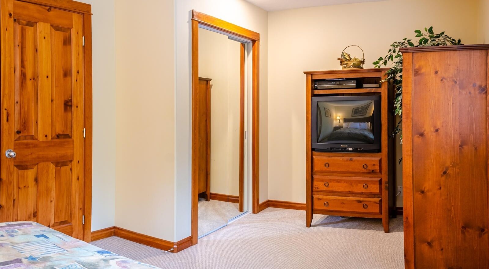 A bedroom with a wooden wardrobe, a television, and a bed with a patterned bedspread.