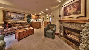 A spacious living room with a fireplace, a sofa, a coffee table, and a dining area in the background. - Timberline Village #38 By Bear Country (Sun Peaks)