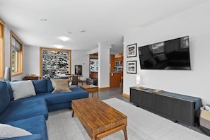 Un salon moderne avec un canapé bleu, une table basse en bois et un grand téléviseur à écran plat fixé au mur.