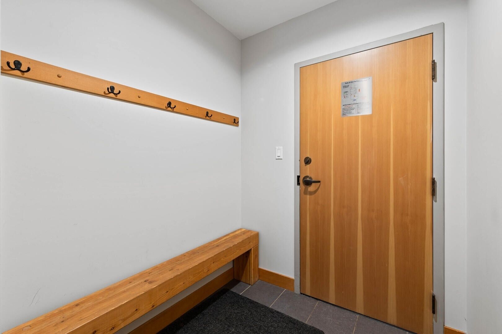 Un pasillo con un banco de madera, un perchero y una puerta de madera con un letrero.