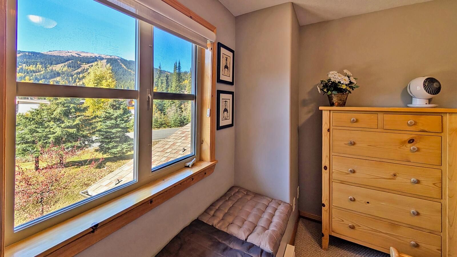 Habitación con un ventanal amplio que ofrece vistas a un paisaje boscoso, un aparador de madera y un banco.