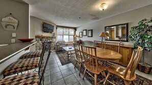 A dining area with a stone fireplace, a television mounted above it, and a large window providing natural light.
