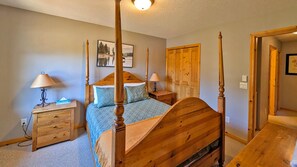 A bedroom with a four-poster bed, wooden nightstands, a dresser, and a door with a wooden panel.
