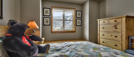 Een slaapkamer met een bed, een houten dressoir, een raam met uitzicht op besneeuwde bergen en lijstwerken aan de muur.