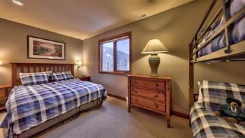 A bedroom with a bed, a nightstand, a dresser, a window, and a lamp.