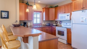 Una cocina con gabinetes de madera, un refrigerador blanco, una estufa, un microondas y una zona de comedor con sillas de madera.
