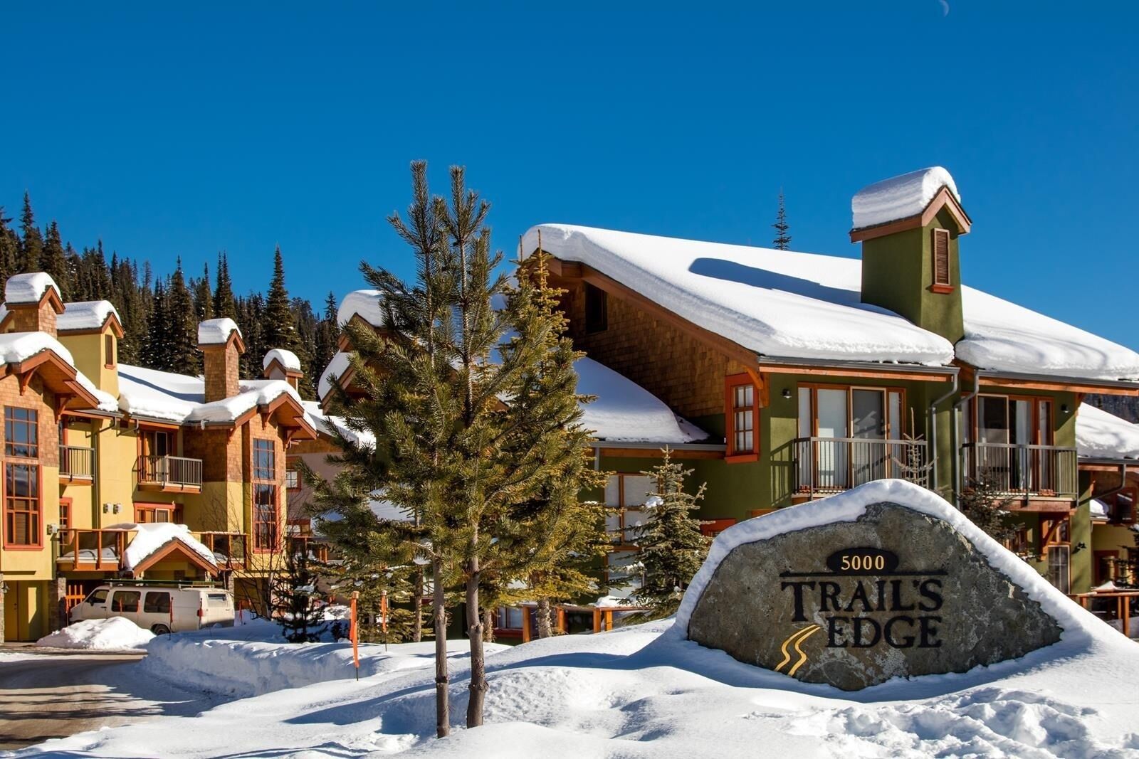 A snow-covered lodge with a stone sign reading "5000 Trails Edge."