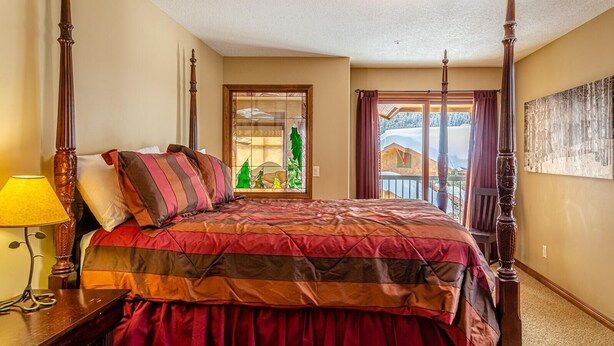 Ein Himmelbett mit Steppdecke, ein Nachttisch mit Lampe und Blick auf eine verschneite Landschaft durch ein Fenster.