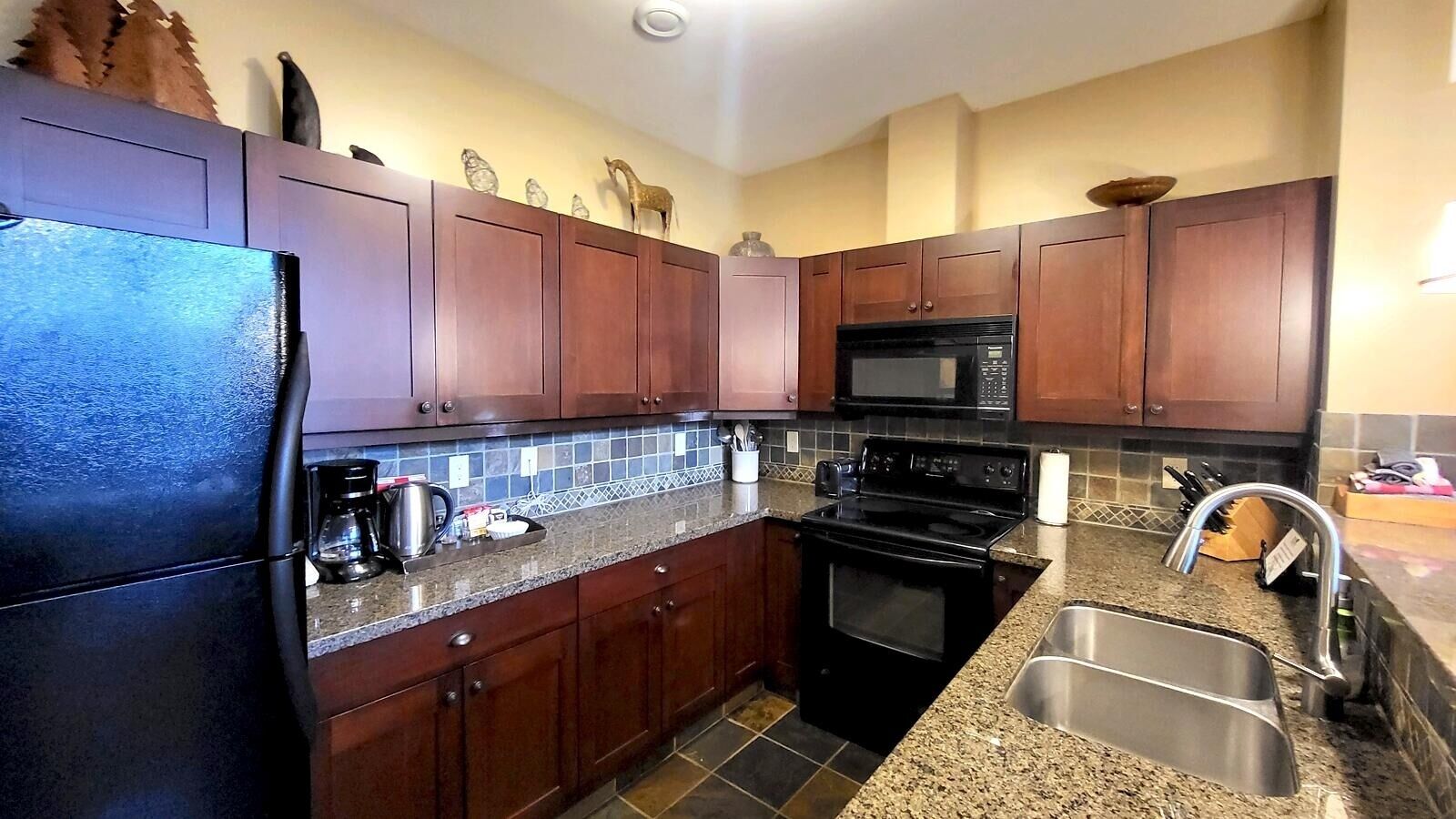 A kitchen with dark wooden cabinets, a black stove, a microwave, a sink, and a coffee maker.