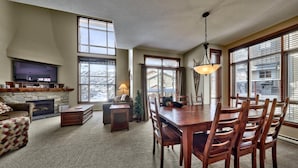A spacious living room with a fireplace, a television, and a dining area with wooden chairs and a table. - Trappers Landing #27 (Sun Peaks)