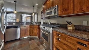 A modern kitchen with wooden cabinets, stainless steel appliances, granite countertops, and pendant lighting. - Trappers Landing #27 (Sun Peaks)