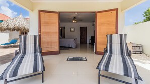 A room with two striped lounge chairs, a bed, and a ceiling fan. - Grand home with a private pool, close to beach (Noord)