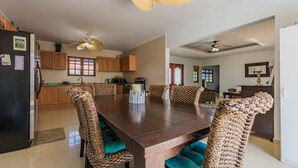 A modern kitchen with wooden cabinets, a dining table with chairs, and a ceiling fan. - Grand home with a private pool, close to beach (Noord)