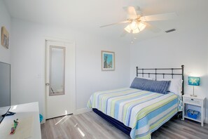 A bedroom with a bed, a nightstand, a ceiling fan, a door, and a wall-mounted picture. - Cape Coral Home w/ Spacious Patio & Private Pool! (Cape Coral)