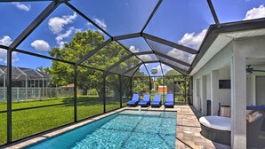 A swimming pool with clear water, surrounded by a covered area with lounge chairs and a seating area.