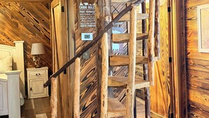 Ein Innenraum einer Holzhütte mit einer Wendeltreppe aus Holz, einem Schild mit Hausregeln und einem rustikalen Holzboden.