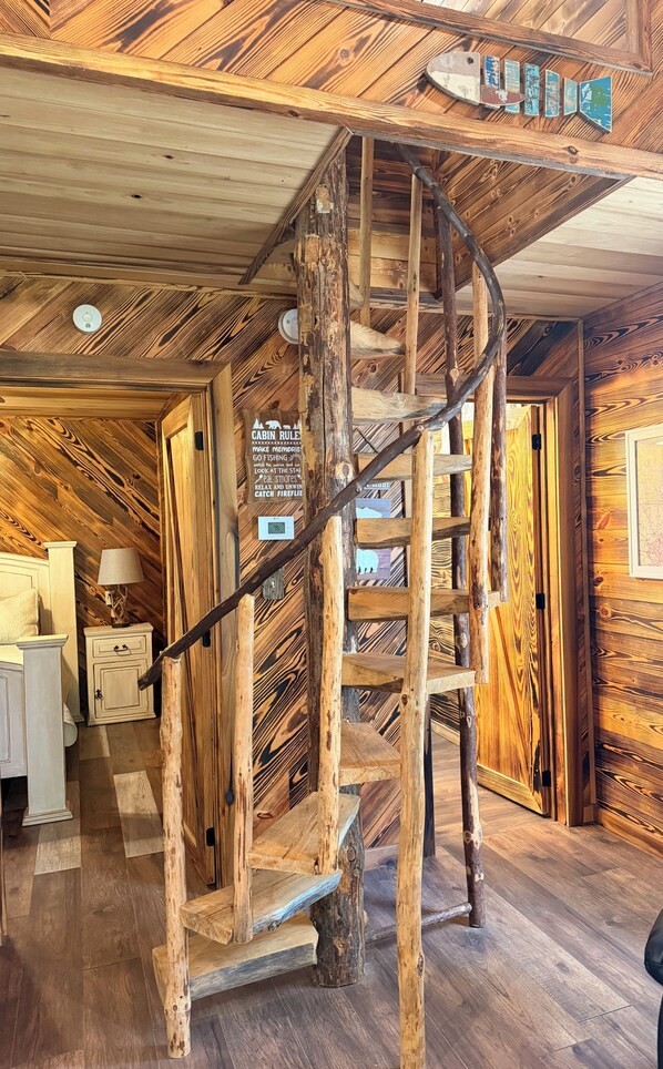 L’intérieur d’une cabane, avec un escalier en colimaçon en bois, un panneau affichant les règles à respecter dans la cabane et un plancher en bois rustique.