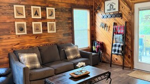 Ein gemütliches Cabin-Interieur mit Holzbalkendecke, einem braunen Ledersofa, einem Couchtisch mit Fernbedienung und gerahmten Bildern an der Wand.